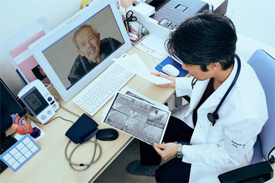Doctor reviewing papers sitting at a computer screen while in telemed meeting with a patient